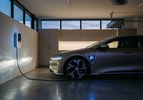 רכב חשמלי מחובר לעמדת טעינה ביתית מודרנית בחניה פרטית